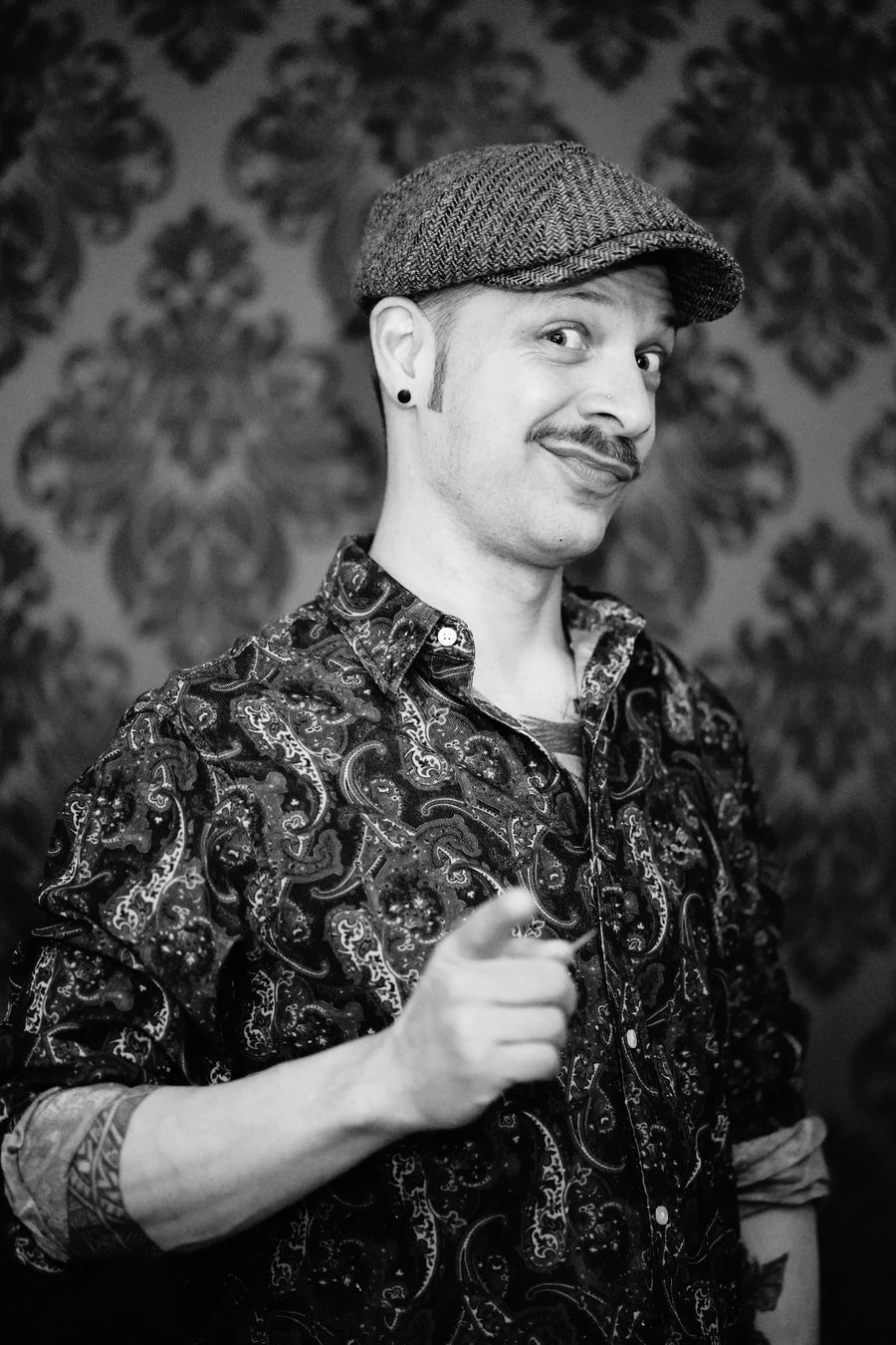 Max Firreri, Barbier und Inhaber von Mad Max Barber, mit Schiebermütze vor der Tapete seines Ladens